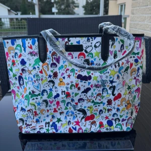 Ny Färgglad väska / bag - Helt ny stor och rymlig väska med ett unikt, färgglatt mönster av ansikten, hjärtan och stjärnor på vit bakgrund. Väskan har svarta handtag och detaljer, samt randigt innerfoder i svart och vitt. Magnetlås. Finns på Hägerstensåsen i Stockholm. 