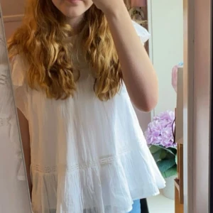 Vit volangblus från Gina Tricot - Superfin vit blus från Gina Tricot med volangdetaljer på ärmarna och nertill. Blusen har en lös passform, rund halsringning och är tillverkad i ett lätt luftigt tyg. 