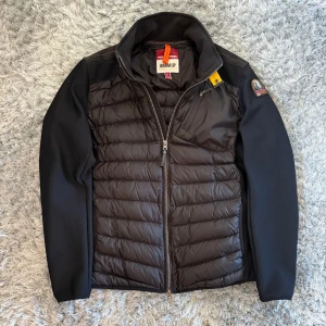 Svart pufferjacka Parajumpers L Cardigan  - Snygg svart pufferjacka från Parajumpers i storlek L. Jackan har quiltad front och rygg, släta svarta ärmar och coolt märke på axeln. Dragkedja framtill och bakficka med zip. Perfekt för dig som gillar stilren och sportig look.