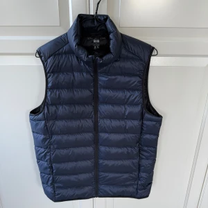 Mörkblå dunväst från Uniqlo - Säljer en mörkblå dunväst från Uniqlo Ultra Light Down. Västen är näst intill oanvänd och det finns inga defekter utan är i perfekt skick. Nypris 599. 