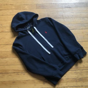 Marinblå hoodie från Polo Ralph Lauren - Säljer en snygg marinblå hoodie från Polo Ralph Lauren i stl M. Passar dig mellan 173-185cm lång. Tröjan är Tillverkad i mjuk bomull. Tröjan är i nyskick och enbart testad alla tags kvar! Nypris 2000 mitt pris 1299kr.