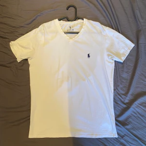 t-shirt från Polo Ralph Lauren - Vit t-shirt från Polo Ralph Lauren i storlek L. T-shirten har den ikoniska broderade Polo-loggan i marinblått på bröstet. Tillverkad i mjuk bomull för skön känsla och clean look.