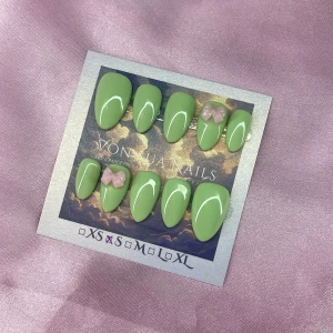 Kiwi 🥝 (S);Short Almond - Snygga handgjorda press-on naglar i en pastellfärgad ljusgrön med glansig finish. Två av naglarna har söta ljusrosa 3D-rosetter som detalj. Naglarna är mandelformade och kommer i S: 15 mm, 11,5 mm, 12 mm, 11 mm, 9 mm , mät innan köp för perfekt passform. Perfekt för dig som vill ha en unik och trendig look.