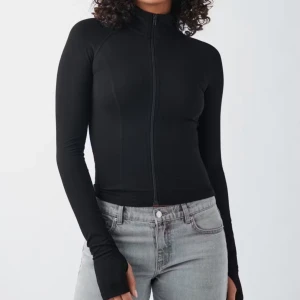 Ziptröja från Gina Tricot - Slimmad svart tröja från Gina Tricot med hel dragkedja framtill och hög krage. Långärmad modell i mjukt, stretchigt material som sitter snyggt på kroppen. Perfekt att styla med jeans eller leggings för en clean look.