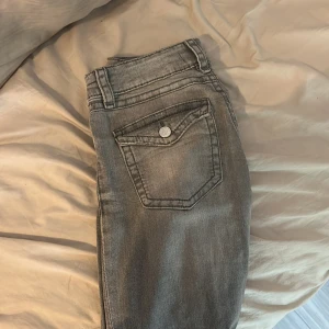 Grå jeans från Gina Tricot - Snygga lågmidjade, utsvängda grå jeans från Gina Tricot med klassisk femficksdesign och silverfärgade knappar. Jeansen har en rak passform och normal midja, tillverkade i mjukt bomullsmaterial med lite stretch för extra komfort. Perfekta för en chill och stilren look.