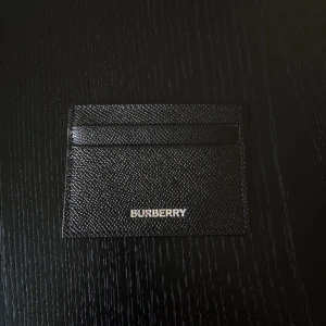 Burberry korthållare  - Slimmad svart plånbok från burberry i exklusiv präglad skinn med silvrig logga framtill. Perfekt för kort, cash osv, stilren och enkel design som passar i fickan. Snygg accessoar för dig som gillar lyxiga detaljer. Helt ny och oanvänd 100% äkta. Ny kostar cirka 2500-3000 i butik.