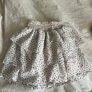 Prickig volangkjol - Supersöt kort kjol med svartprickigt mönster på vit botten. Storlek 134/140 men skulle säga att man kan ha den uppåt i storlekar också 