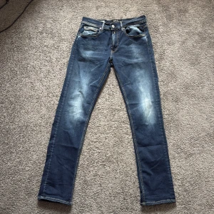 Replay Hyperflex Grover  - Snygga Replay Hyperflex Grover jeans i mörkblå tvätt med coola slitningar framtill. Klassisk femficksmodell med kontrastsömmar och läderpatch bak. Stretchigt material som sitter skönt och följer kroppen. Perfekt för dig som gillar stilrena och moderna jeans.
