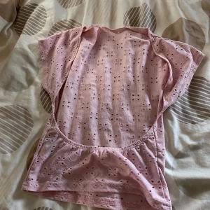 Ljusrosa broderad blus med hålmönster - Säljer en ljusrosa blus med korta ärmar och broderat hålmönster över hela toppen. Modellen är loose fit och har en söt, feminin vibe med små broderade detaljer. Perfekt för dig som gillar romantiska och luftiga plagg.