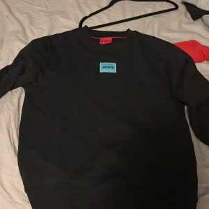 Svart tröja från Hugo - Säljer en stilren svart tröja från Hugo med en liten logotyp på bröstet. Tröjan har långa ärmar och en klassisk rund halsringning. Perfekt för en avslappnad look.