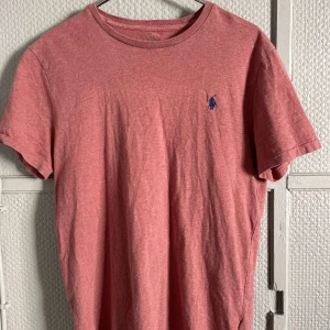 Röd t-shirt från Ralph Lauren - Säljer en snygg röd t-shirt från Ralph Lauren med en liten blå broderad logga på bröstet. T-shirten har en klassisk rund hals och korta ärmar. Perfekt för en avslappnad stil.