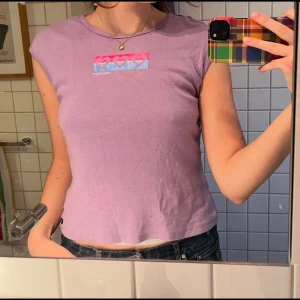 Lila topp från Tommy Hilfiger - Supersöt lila topp från Tommy Hilfiger Jeans med ett tryck av hjärtan i rosa och blått på bröstet. Toppen har korta ärmar och en rund halsringning. Passar som M, mycket fint skick! 