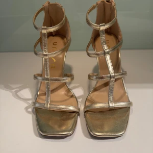 Guldiga sandaler med klack och dragkedja - Snygga guldiga sandaler med klack och flera remmar. De har en dragkedja baktill för enkel på- och avtagning. Perfekta för att ge en glamorös touch till din outfit.