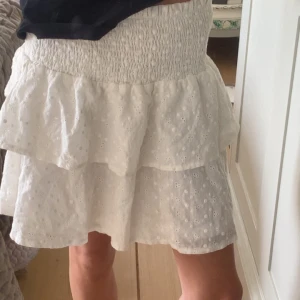 Vit kjol - Säljer en söt vit kjol från Chelsea med volanger och broderade detaljer. Kjolen är i mycket bra skick och knappast använd, den går även att använda som topp. perfekt för sommaren💕