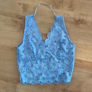 Blå spetslinne - Säljer ett vackert blått spetslinne. Toppen har ett blommigt mönster och en v-ringad framdel. Perfekt för sommarens varma dagar eller en festlig kväll.
