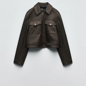 Brun skinnjacka - Snygg brun/grön skinnjacka med en croppad design och långa ärmar. Jackan har knappar framtill och två bröstfickor med lock. Perfekt för en stilren look.