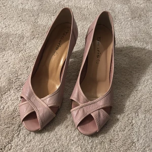 Rosa pumps från Tamaris - Snygga rosa pumps från Tamaris med öppen tå och klack. Skorna har en elegant design med korsade remmar framtill. Perfekta för en stilren look. Lite sex and the city vibe #miranda #slay🫶🏻 Frakt tillkommer