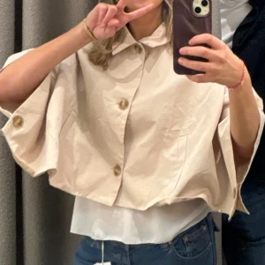 Beige kappa med knappar - Snygg beige poncho med stora knappar framtill. Den har en lös passform och trekvartsärmar, perfekt för en stilren look. Passar bra till både jeans och klänning. 
