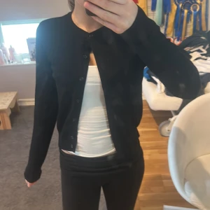 Svart kofta från H&M - Säljer en klassisk svart kofta från H&M. Den har långa ärmar och knappar framtill. Perfekt för lager-på-lager och passar till många olika outfits.