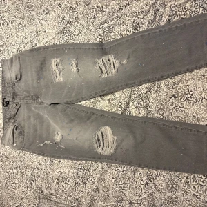 Grå jeans med slitningar för ett bra pris  - Säljer ett par grå jeans med coola slitningar och färgstänk. De har en normal passform och är perfekta för en avslappnad stil. Passar bra till sneakers eller boots.