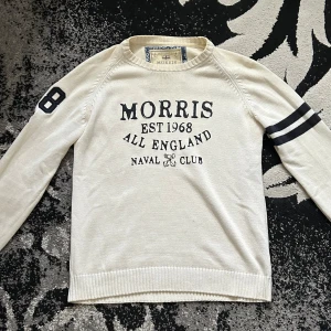 Vit tröja från Morris - Säljer en vit tröja från Morris med texten 'Morris Est 1968 All England Naval Club' på framsidan. Tröjan har långa ärmar med en svart rand och siffran 8 på ena ärmen. Tillverkad i 100% bomull.