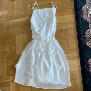 Vit klänning från Elise Ryan - Säljer en elegant vit klänning från Elise Ryan med smala axelband och vackra blommiga detaljer. Klänningen har en luftig passform och är perfekt för sommarens festligheter. Den har en fin längd som slutar ovanför knäna och ger en romantisk känsla.