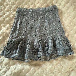 Blommig kjol från Lindex - Söt ljusblå kjol från Lindex med små vita blommor och volangdetaljer. Perfekt för en somrig look. Elastisk midja för extra komfort.