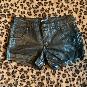 Svarta skinnshorts  - Snygga svarta skinnshorts. De har en klassisk femficksdesign och en stilren look. Perfekta för en edgy stil!