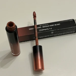 MAC Love Me Liquid Lipcolour i nyansen Feel Me? - Snygg flytande läppfärg från MAC i nyansen Feel Me?. Den har en elegant förpackning med en gradient av svart och koppar. Perfekt för att ge läpparna en intensiv och långvarig färg.