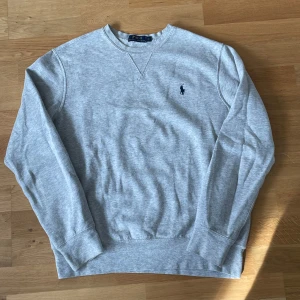 Grå tröja från Polo Ralph Lauren - Säljer en klassisk grå tröja från Polo Ralph Lauren med rund halsringning och broderad logotyp på bröstet. Priset kan diskuteras vid snabb affär!