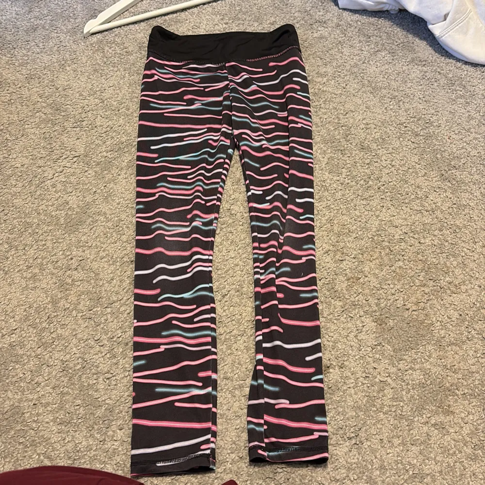 Säljer ett par färgglada leggings med vågigt mönster i rosa, blått och vitt på svart bakgrund. Ett par perfekta träningsbyxor för barn helt enkelt. Storlek 134-140. 🤍. Farkut & Housut.