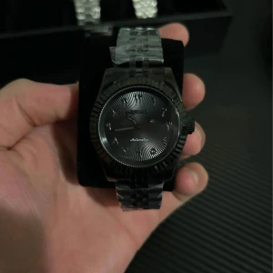 Svart automatisk klocka - Snygg svart automatisk klocka från Seiko med arabiska siffror på urtavlan. Klockan har en stilren design med en svart länkarmband och en mörk urtavla. Perfekt för den som gillar en elegant och modern stil.
