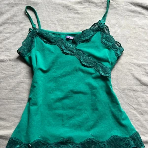 Grön linne med spetsdetaljer från Zola - Snygg grön linne med smala axelband och vackra spetsdetaljer längs halsringningen och nederkanten. Perfekt för en somrig look eller som ett lager under en tröja. Axelbanden är justerbara för bästa passform. Pris kan diskuteras!💓