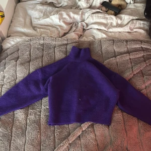 Lila stickad tröja från Zara - Säljer en snygg lila stickad tröja från Zara. Tröjan har en hög krage och långa ärmar, perfekt för kyligare dagar. Den är croppad och ger en trendig look. Passar utmärkt till både jeans och kjol. 💜