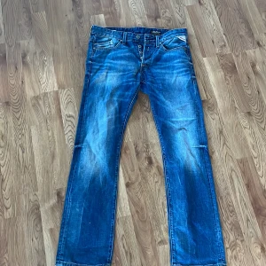 Blå jeans från Replay - Säljer ett par snygga blå jeans från Replay, modell Waitom. De har en klassisk femficksdesign och knappar i gylfen. Perfekta för en avslappnad stil. Och på höger och vänster ficka har dem slitningar 