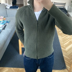 Olivgrön stickad tröja från Peak Performance - Säljer en snygg olivgrön stickad tröja från Peak Performance. Tröjan har en dragkedja framtill och en stilren design med ribbade detaljer. Perfekt för kyligare dagar. 🧥