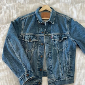 Blå jeansjacka från Levi's - Säljer en klassisk blå jeansjacka från Levi's med bruna knappar och två bröstfickor. Jackan har en normal passform och är perfekt för vår och sommar. 