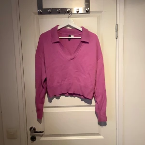 Rosa v-ringad tröja - Säljer en snygg rosa tröja med v-ringning och krage. Tröjan har långa ärmar och en croppad passform som ger en trendig look. Perfekt för att liva upp garderoben!