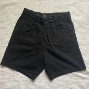 Svarta shorts från H&M - Säljer ett par svarta mjukis shorts från H&M med elastisk midja och snörning. De har en bakficka och två fickor framtill. 