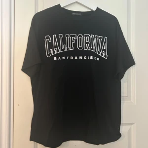 Svart t-shirt California San Francisco - Svart t-shirt från Shein med stor vit text 'California San Francisco' på bröstet. Klassisk passform med rund hals och korta ärmar. Perfekt för en avslappnad streetstyle-look.