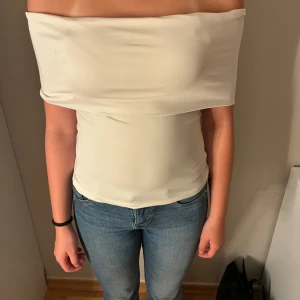 Vit axelbandslös tubtopp - Säljer en stilren vit tubtopp med offshoulder-design. Gjord i mjukt och stretchigt material som sitter skönt mot kroppen. Jag säljer denna för den inte kommer till användning!❤️