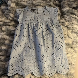 Ljusblå broderad blus - Supersöt ljusblå blus  med broderade detaljer och vågig nederkant. Blusen är ärmlös med volang vid axlarna och har ett luftigt, somrigt snitt. Perfekt för varma dagar och ger en romantisk känsla.