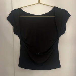 Svart rygglös topp - Svart topp från Stradivarius som är öppen i ryggen. Tröjan är kortärmad och i mycken bra skick. Endast använd ett fåtal gånger då jag inte riktigt tyckte den passade mig
