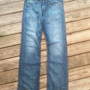 Levi's 506 blå jeans straight fit -  Levi's 506 jeans i blå denim med raka ben och normal passform. Snyggt slitna detaljer och femficksmodell. Tidlös look med orange sömmar och knappgylf. Perfekta till sneakers eller boots.