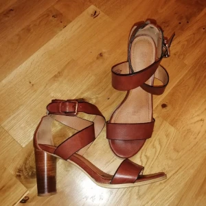 Bruna sandaler med klack och remmar - Snygga bruna sandaler med breda remmar i skinnimitation och rund tå. Skorna har en stabil hög klack och justerbart spänne vid ankeln. Storlek 36,men skulle även passa en 37.