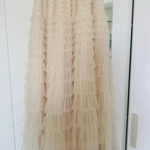 Beige volangkjol i tyll - Supersöt långkjol i beige tyll med massor av volanger som ger en riktigt fluffig och drömmig look. Perfekt för dig som vill sticka ut. Resår i midjan för extra bekvämlighet. Helt oanvänd. Den är köpt för 799kr men jag säljer den för 500 otroligt bra pris! Köpt på copenhagen Luxe
