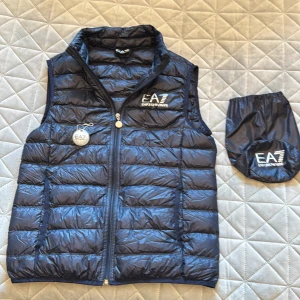 EA7 Emporio Armani pris är rörligt,  tunn dunväst - ⚠️Diskuterbart pris ⚠️Snygg mörkblå dunväst med allt originalt från EA7 Emporio Armani med quiltad design och hög krage. Västen har dragkedja framtill, två sidofickor och tydlig logga på bröstet. Tillhörande förvaringspåse medföljer. Skicka vid frågar