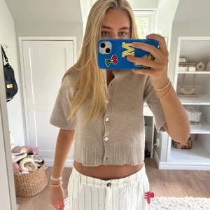 Beige kofta från & Other Stories - Superfin beige kofta från & Other Stories med crop kort ärm. Tröjan har ribbade detaljer vid hals och nederkant samt knappar framtill. Perfekt till lager-på-lager och enkel att styla med både jeans och kjol.💕