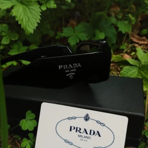 Svarta solglasögon från Prada - Snygga svarta solglasögon från Prada med breda skalmar och rektangulära bågar. Glasögonen har en stilren och chunky design med Pradas logga i silver på sidan. Kommer med originaletui, putsduk och äkthetskort. Skriv för fler bilder