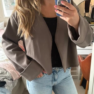  Overshirt/jacka från Gina Tricot - Säljer en brun overshirt från Gina Tricot med omlott-design och breda ärmar. Endast använd en gång därav ny skick. Jackan är croppad och har dekorativa sömmar längs kanterna och ärmsluten. Perfekt att slänga över en t-shirt eller ha som en jacka på sen sommaren! Nypris 500kr